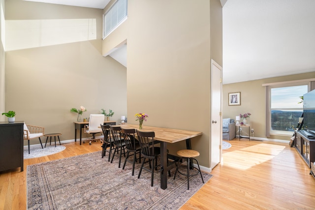 dining space featuring high vaulted ceiling, baseboards, and wood finished floors