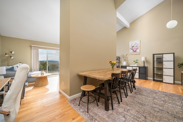 dining space featuring wood finished floors, baseboards, and high vaulted ceiling