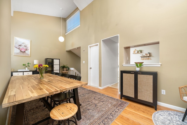 dining area featuring baseboards, wood finished floors, and a towering ceiling