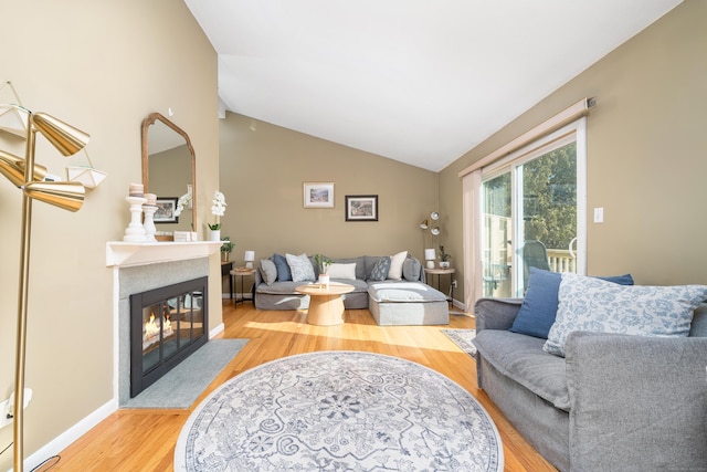 living room featuring light wood finished floors, a fireplace with flush hearth, baseboards, and lofted ceiling