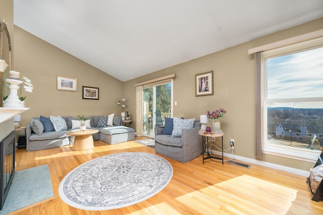 living area featuring wood finished floors, baseboards, visible vents, lofted ceiling, and a fireplace with flush hearth