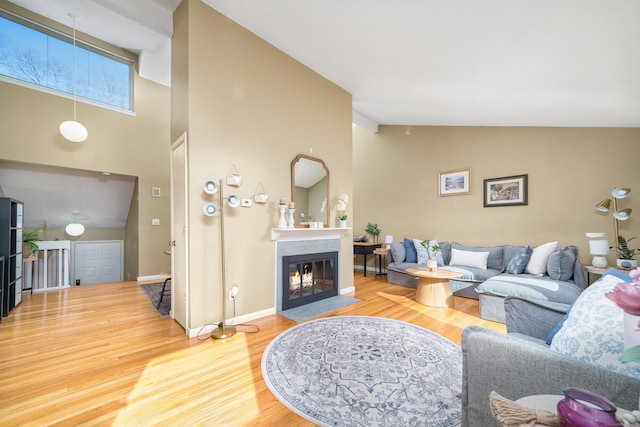 living area with a multi sided fireplace, high vaulted ceiling, baseboards, and wood finished floors