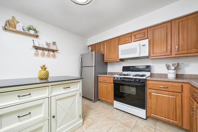 kitchen featuring light tile patterned floors, brown cabinetry, white microwave, freestanding refrigerator, and gas range oven