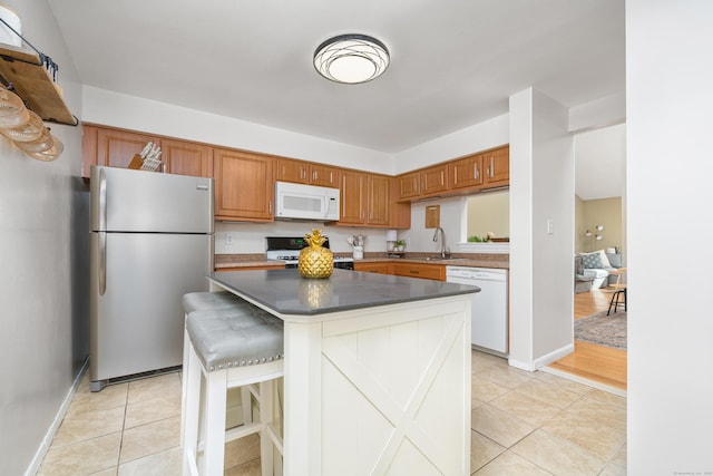 kitchen featuring white appliances, light tile patterned flooring, brown cabinetry, and a center island