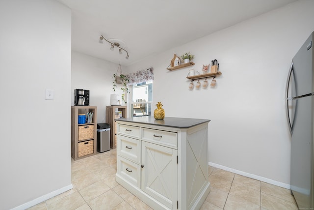 kitchen featuring light tile patterned floors, baseboards, dark countertops, and freestanding refrigerator