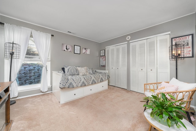 bedroom featuring baseboards, visible vents, two closets, and light carpet