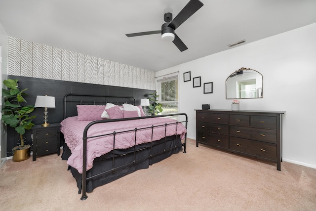 bedroom with visible vents, baseboards, light colored carpet, ceiling fan, and an accent wall