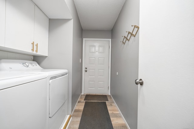 washroom featuring baseboards, light wood-type flooring, cabinet space, a textured ceiling, and separate washer and dryer