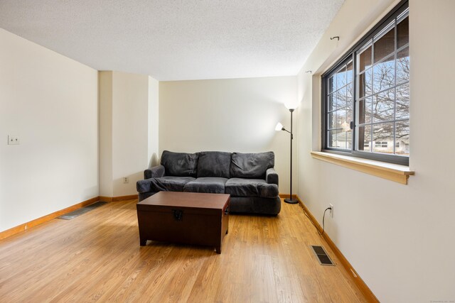 living area featuring baseboards, light wood-style floors, visible vents, and a textured ceiling
