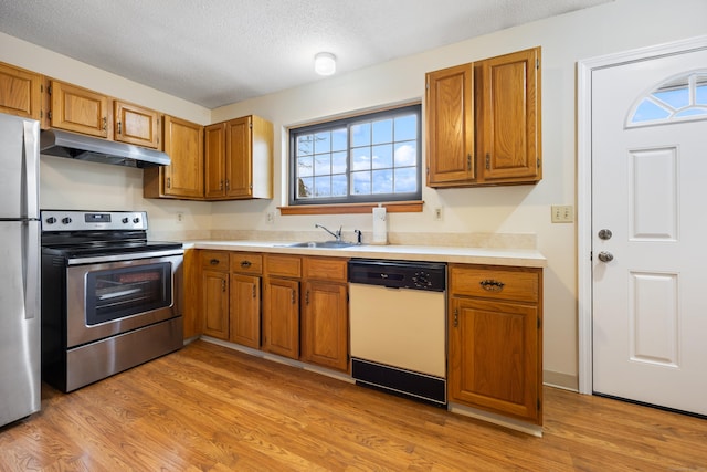 kitchen featuring stainless steel appliances, under cabinet range hood, a sink, and brown cabinets