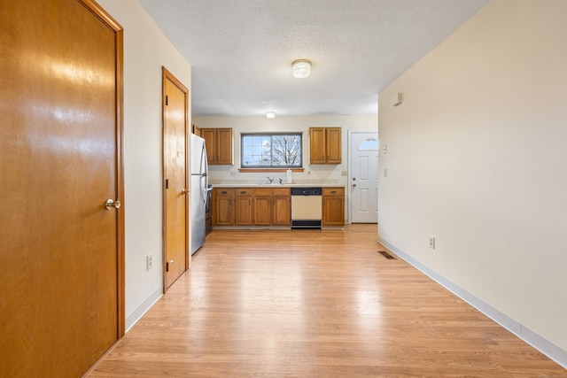 kitchen with light countertops, white dishwasher, freestanding refrigerator, and light wood-style flooring