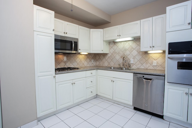 kitchen with decorative backsplash, appliances with stainless steel finishes, white cabinetry, a sink, and light tile patterned floors