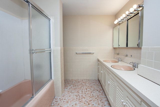 bathroom with tile walls, combined bath / shower with glass door, a sink, and wainscoting