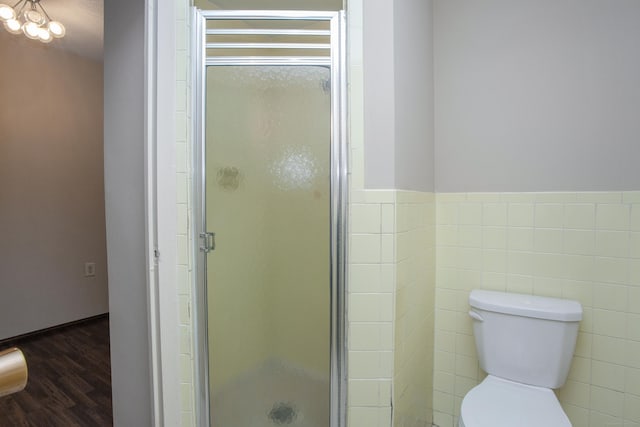 bathroom featuring a stall shower, toilet, wood finished floors, wainscoting, and tile walls