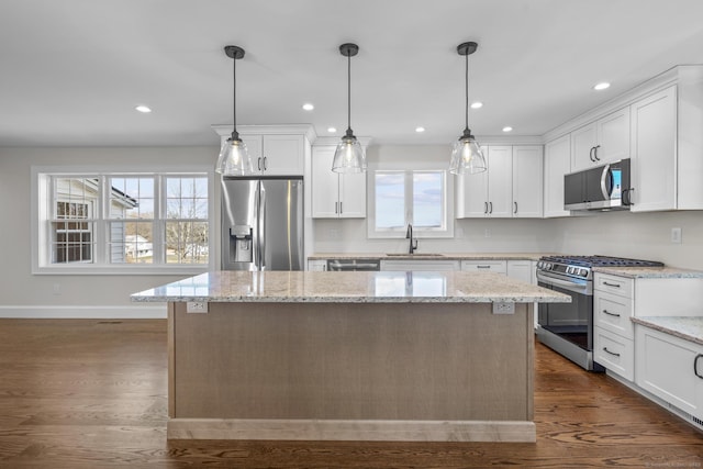 kitchen featuring a kitchen island, dark wood finished floors, a sink, appliances with stainless steel finishes, and white cabinetry