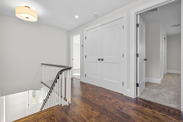 hall featuring wood finished floors, visible vents, baseboards, recessed lighting, and an upstairs landing