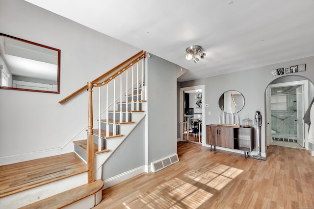 staircase featuring arched walkways, wood finished floors, visible vents, and baseboards