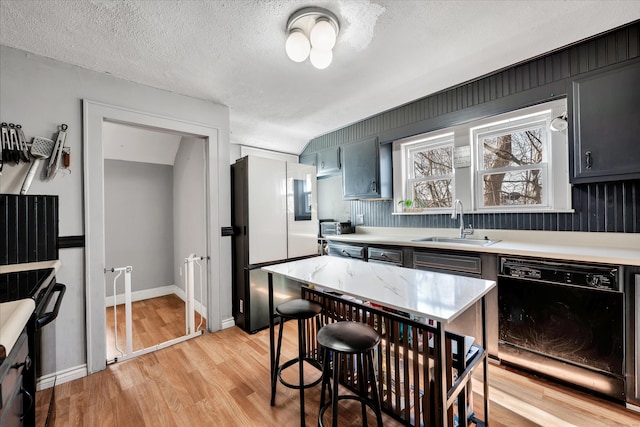 kitchen with a sink, black dishwasher, freestanding refrigerator, light wood finished floors, and light countertops