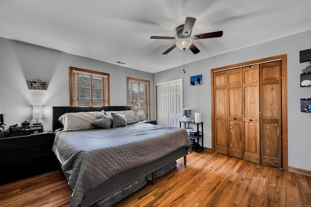 bedroom with baseboards, visible vents, light wood-style flooring, ceiling fan, and two closets