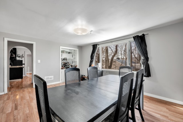 dining space with light wood-type flooring, visible vents, arched walkways, and baseboards