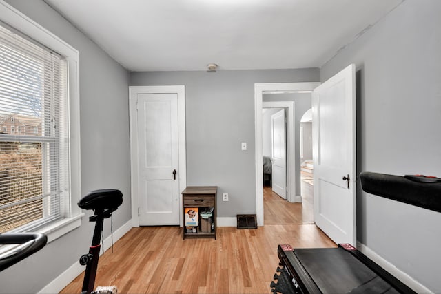 exercise area featuring arched walkways, light wood-type flooring, and baseboards