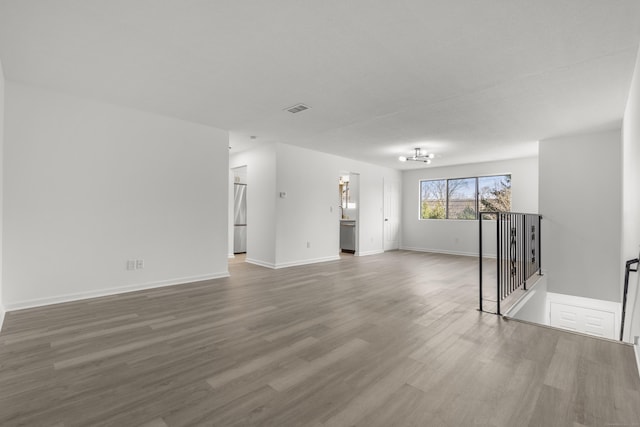 unfurnished living room with a notable chandelier, wood finished floors, visible vents, and baseboards