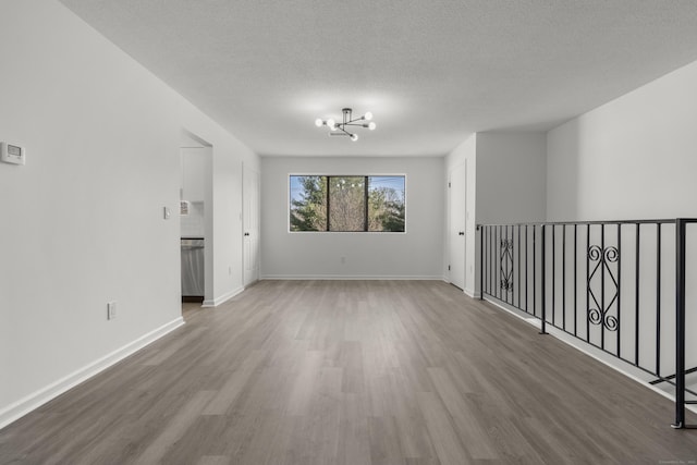 unfurnished room featuring baseboards, a textured ceiling, an inviting chandelier, and wood finished floors