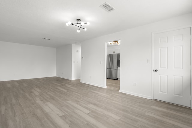 unfurnished room with visible vents, baseboards, light wood-style floors, and a chandelier