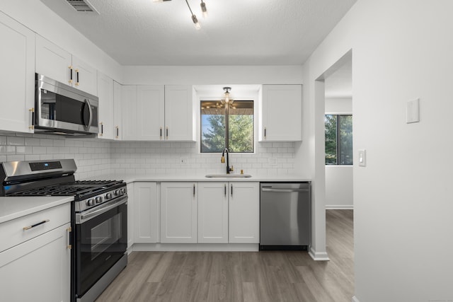 kitchen featuring visible vents, appliances with stainless steel finishes, light wood-style floors, white cabinetry, and a sink