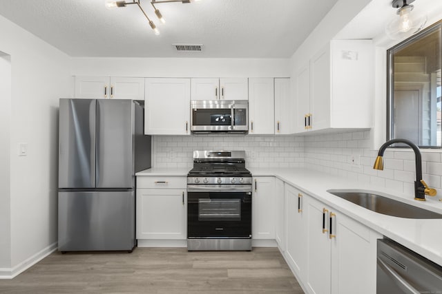 kitchen with visible vents, light wood-style flooring, white cabinets, stainless steel appliances, and a sink