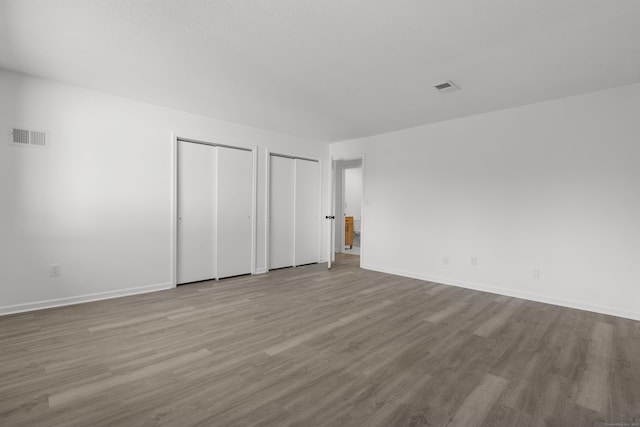 unfurnished bedroom featuring visible vents, two closets, baseboards, and wood finished floors