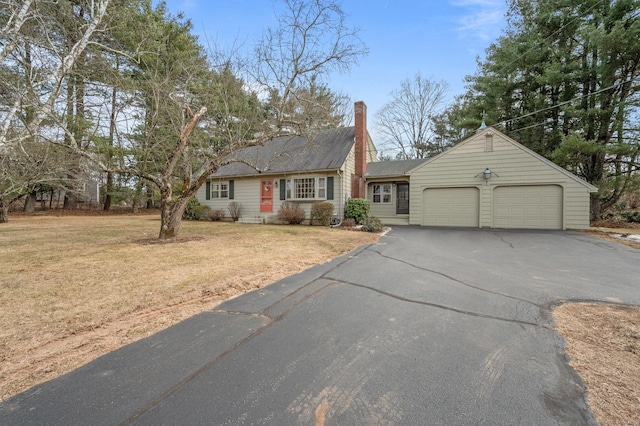 view of front facade featuring a front yard, a garage, driveway, and a chimney