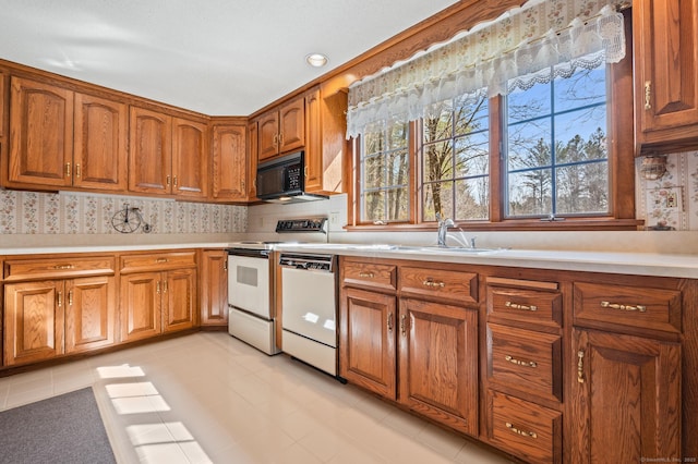 kitchen with brown cabinets, white appliances, light countertops, and a sink