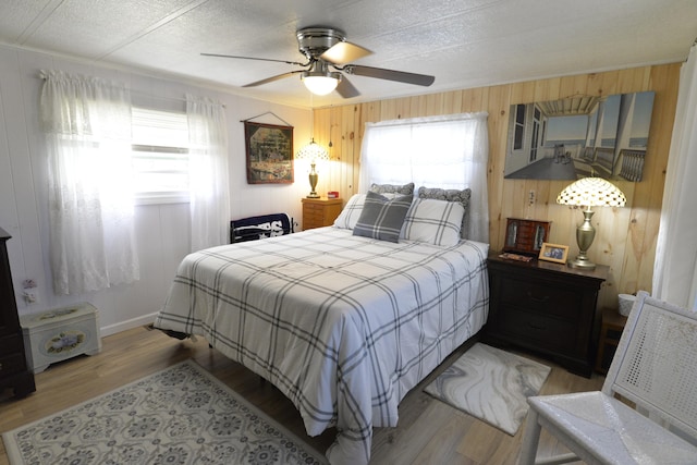 bedroom featuring a ceiling fan, light wood finished floors, ornamental molding, wood walls, and a textured ceiling