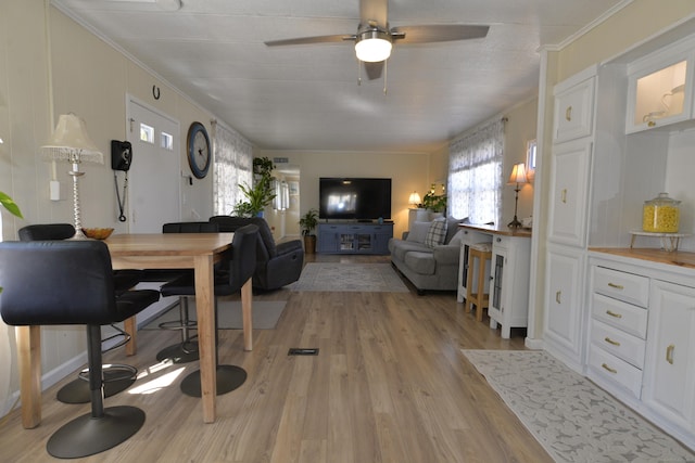 living area featuring light wood-style flooring, crown molding, and a ceiling fan