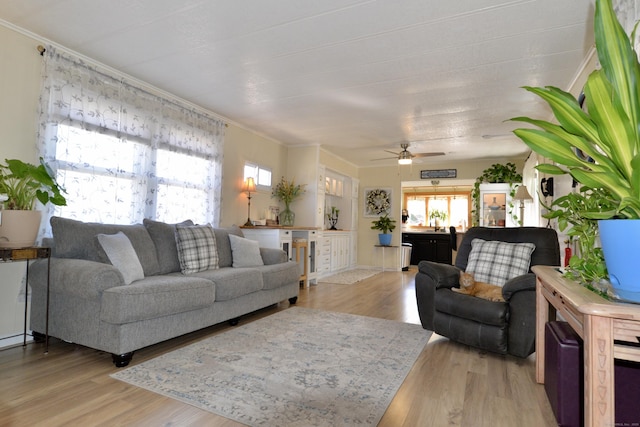 living room with light wood-style flooring, crown molding, and a ceiling fan