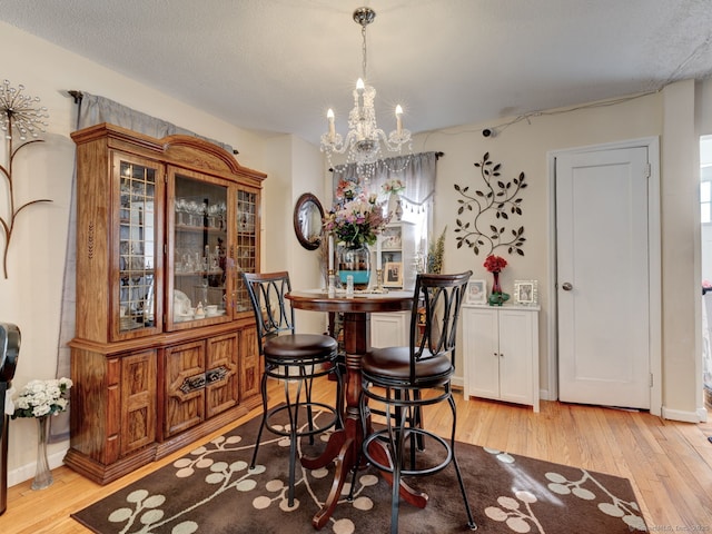 dining space with light wood finished floors, baseboards, a textured ceiling, and an inviting chandelier