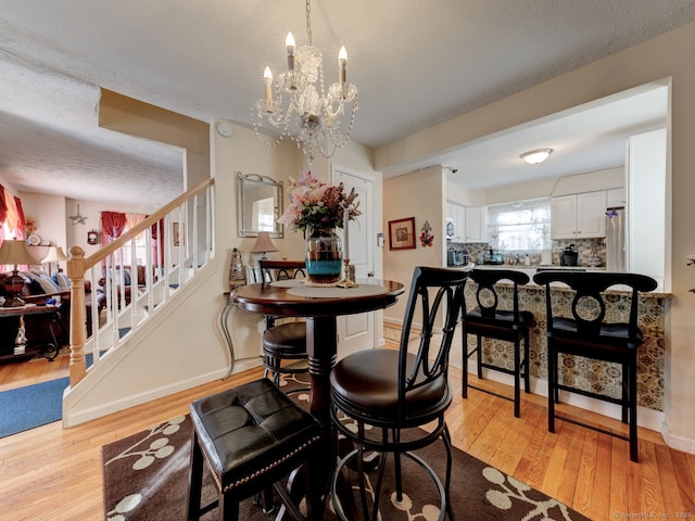 dining space featuring a notable chandelier, light wood-style flooring, stairway, and baseboards