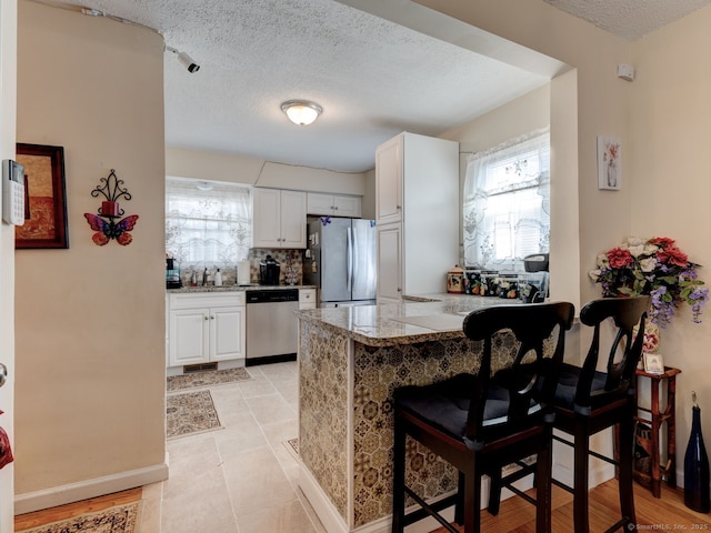 kitchen with a kitchen bar, backsplash, white cabinetry, stainless steel appliances, and a peninsula