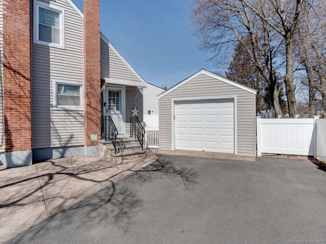 view of front of property featuring fence, aphalt driveway, a chimney, a garage, and an outbuilding