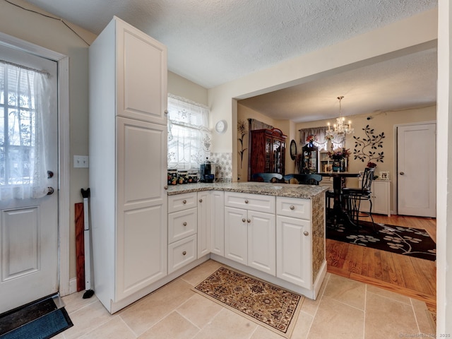 kitchen with light stone counters, light tile patterned floors, an inviting chandelier, a peninsula, and white cabinets