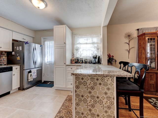kitchen featuring a breakfast bar, white cabinets, stainless steel appliances, and light stone countertops