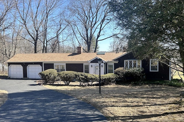 single story home with driveway, a chimney, a garage, and roof with shingles