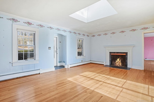 unfurnished living room featuring a baseboard heating unit, a lit fireplace, baseboard heating, a skylight, and wood finished floors