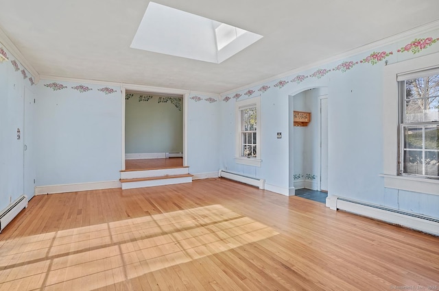 unfurnished room with a healthy amount of sunlight, a baseboard heating unit, and wood finished floors