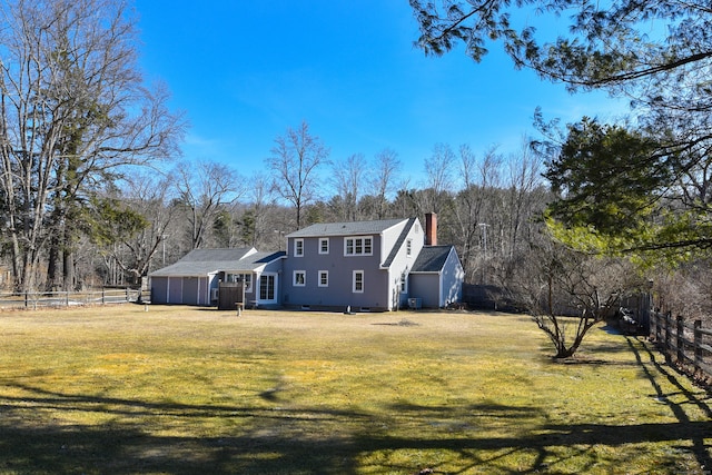 rear view of property with a garage, a chimney, a yard, and fence