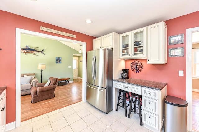 kitchen with freestanding refrigerator, dark stone counters, white cabinets, light tile patterned floors, and glass insert cabinets