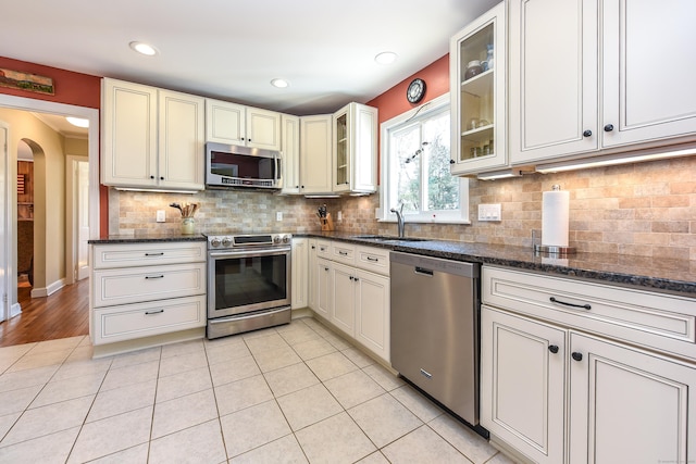 kitchen featuring a sink, dark stone counters, light tile patterned floors, and stainless steel appliances