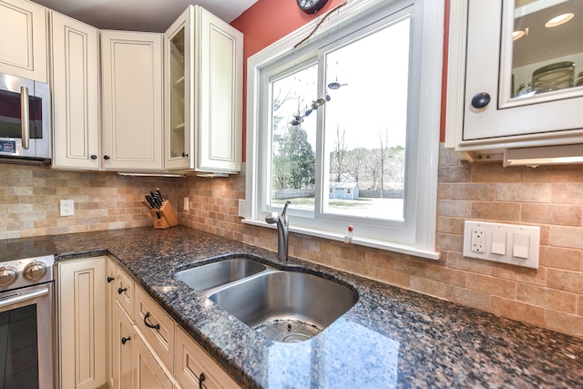 kitchen featuring decorative backsplash, dark stone countertops, stainless steel appliances, and a sink