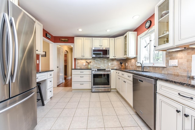 kitchen with a sink, dark stone countertops, tasteful backsplash, appliances with stainless steel finishes, and light tile patterned floors